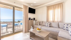 Una sala de estar moderna con un sofá, una mesa de centro y un televisor. Hay un balcón con piscina y mobiliario exterior.