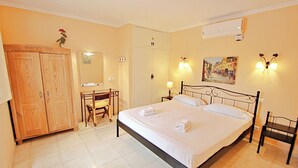 A hotel room with a bed, a desk, a chair, a wardrobe, and a wall-mounted air conditioner.