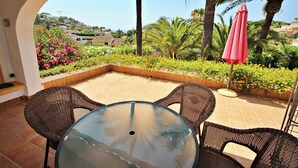 A patio with wicker furniture, a glass table, and a red umbrella.