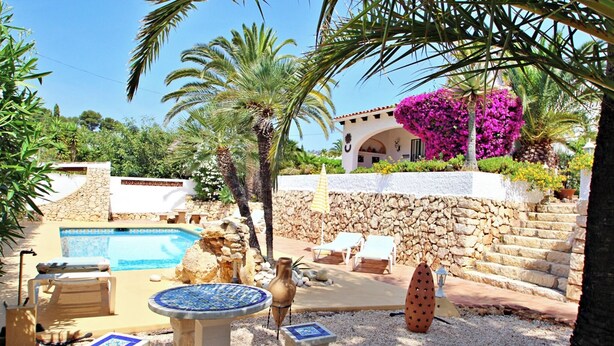 A pool area with a stone wall, lounge chairs, and a decorative table.