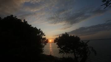 A sunset over a calm body of water with silhouettes of trees framing the view.