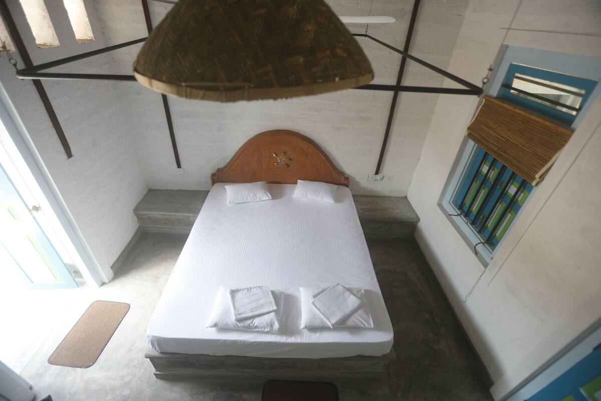 A single bed with white linens and pillows, a wooden headboard, and a hanging light fixture.