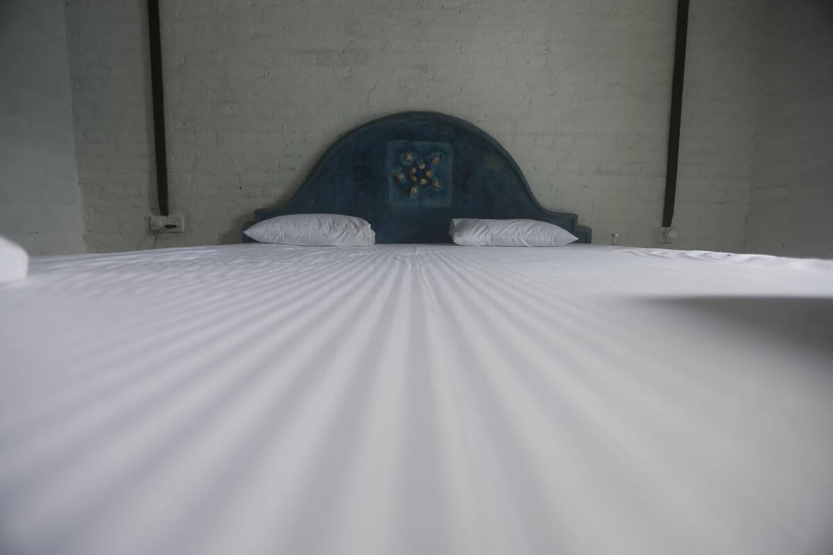 A bed with a wooden headboard and white bedding in a room with plain walls.