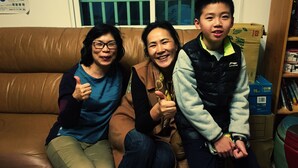 Three people sitting on a brown leather couch in a room with a window and a bookshelf. - Tomato Coffee BnB (Taitung)