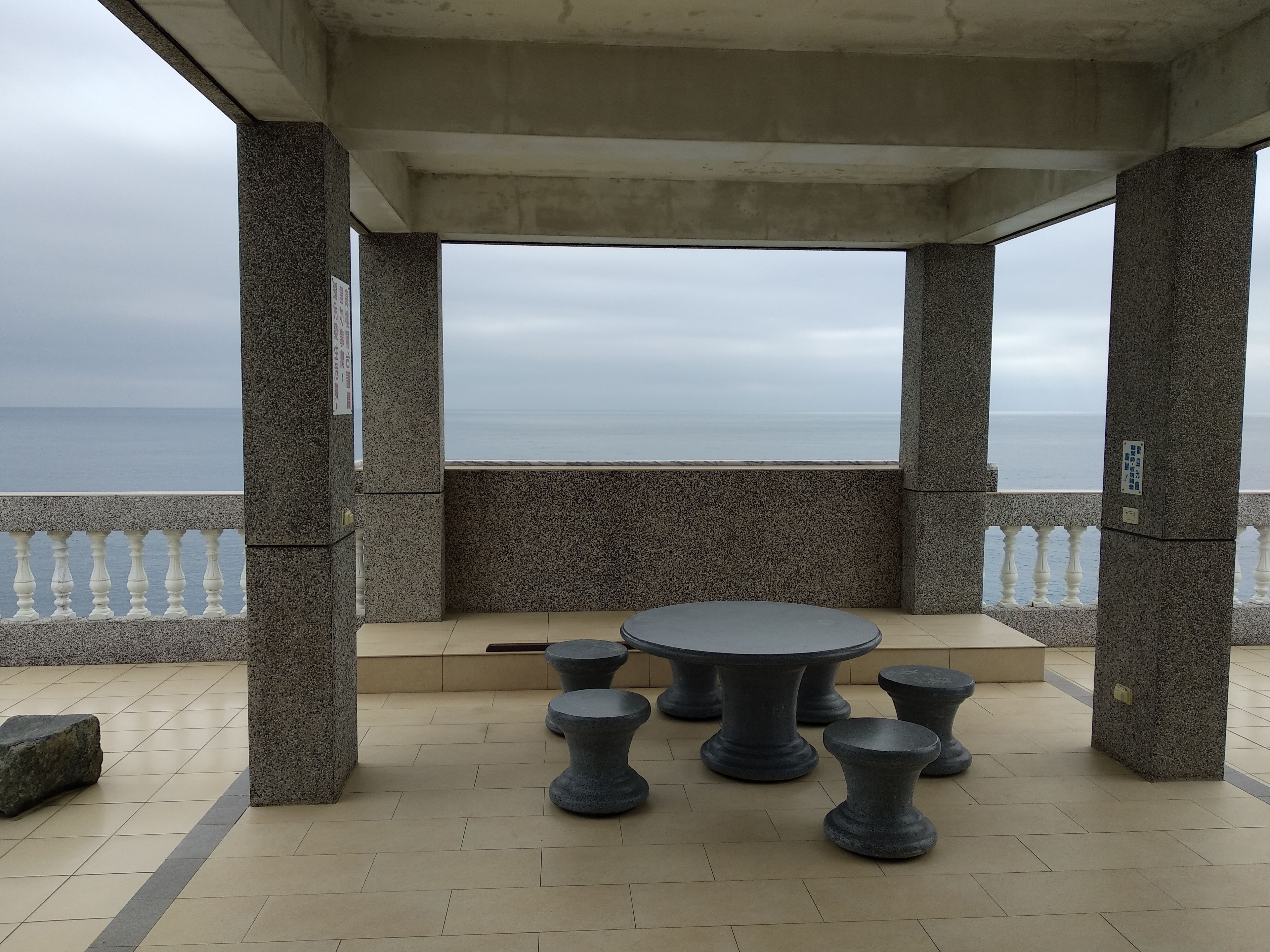 Un espace extérieur abrité, avec une table et des tabourets, offrant une vue sur la mer.