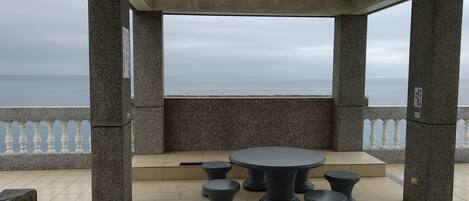 Un espace extérieur abrité, avec une table et des tabourets, offrant une vue sur la mer.