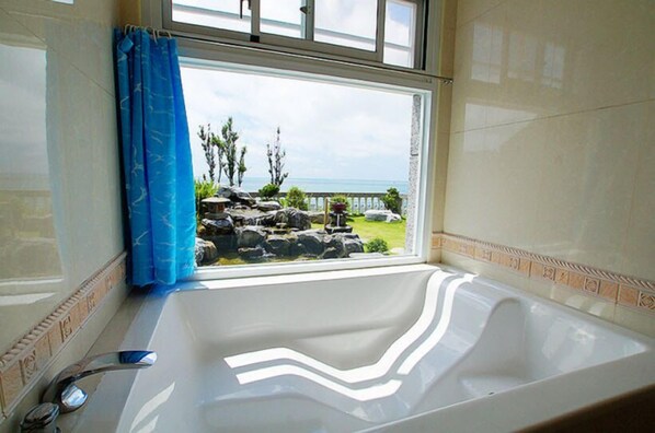 A bathroom with a large bathtub, a window with a view of a rocky garden and the sea. - Sea Bay B&B (Taitung)