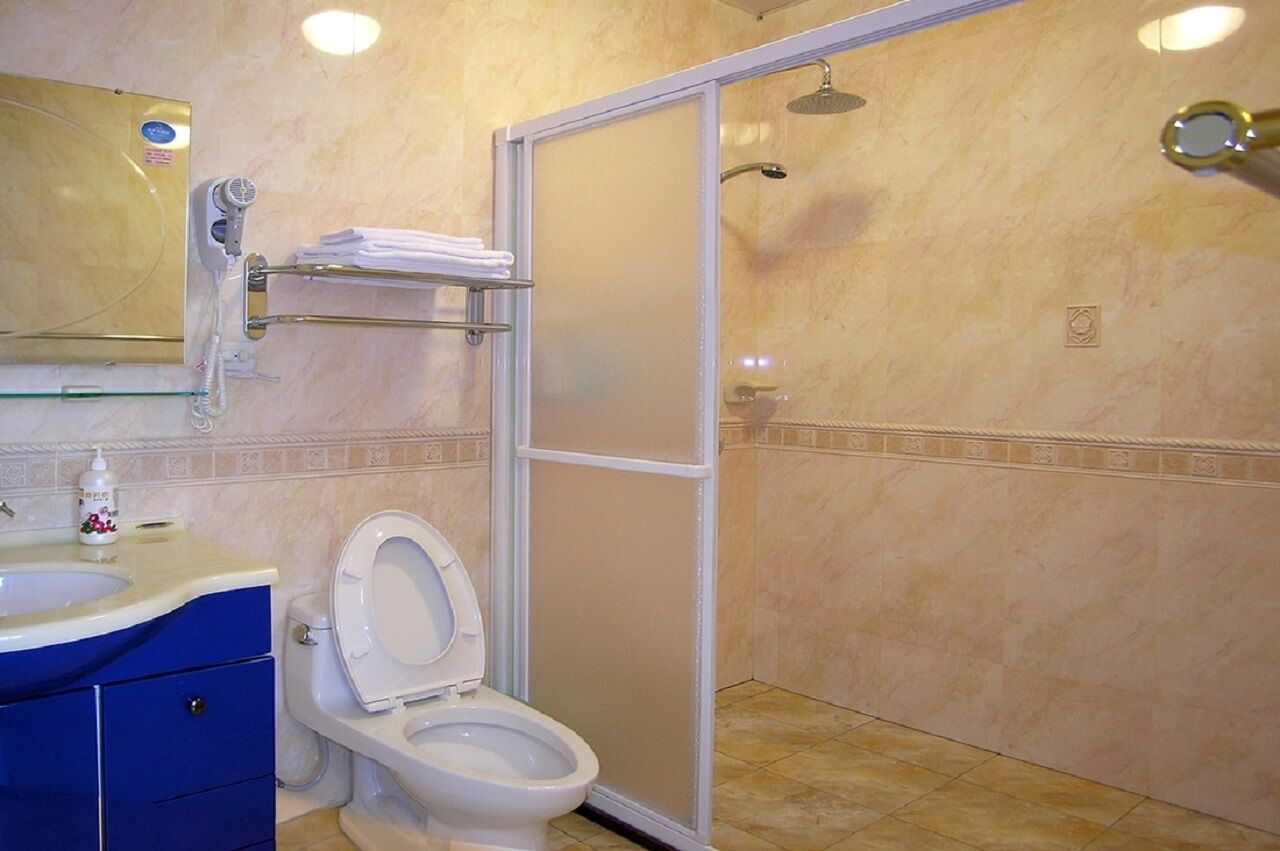 Ein Badezimmer mit Toilette, Waschbecken mit blauem Unterschrank, Handtuchhalter, Duschkabine und Spiegel über dem Waschbecken.