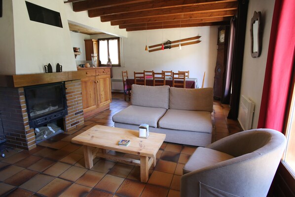 Uma sala de estar acolhedora com lareira, um sofá, uma mesa de centro de madeira e uma área de jantar com cadeiras e uma mesa.