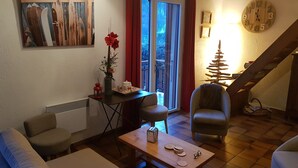 A cozy living room with a sofa, a coffee table, and a chair. There's a painting on the wall, a vase with flowers, and a clock on the wall.