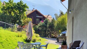 A patio with outdoor furniture, a wooden house in the background, and a car parked nearby.
