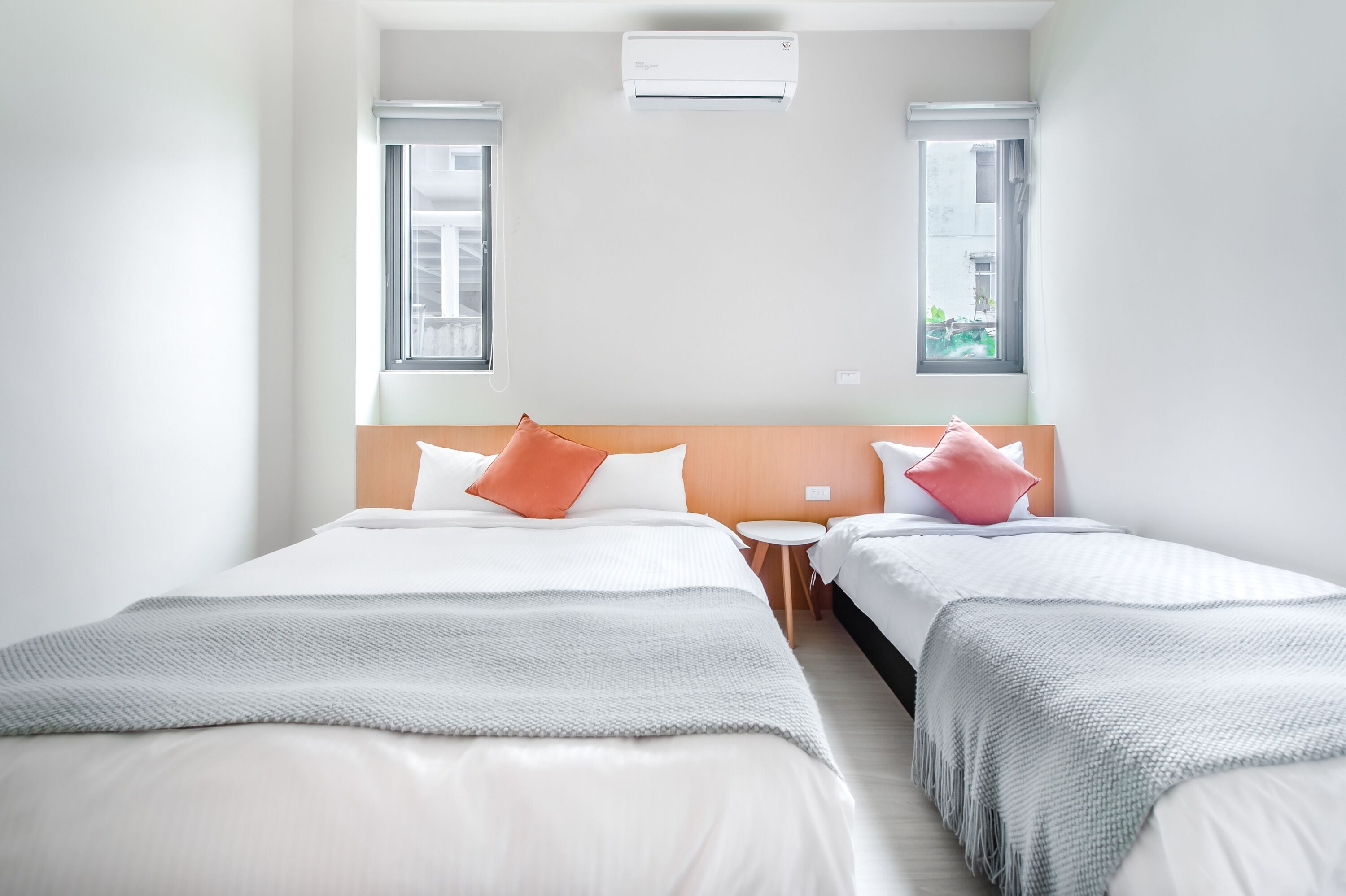 Ein Hotelzimmer mit zwei Betten, einem kleinen runden Tisch und einem Fenster mit Blick auf Gebäude.