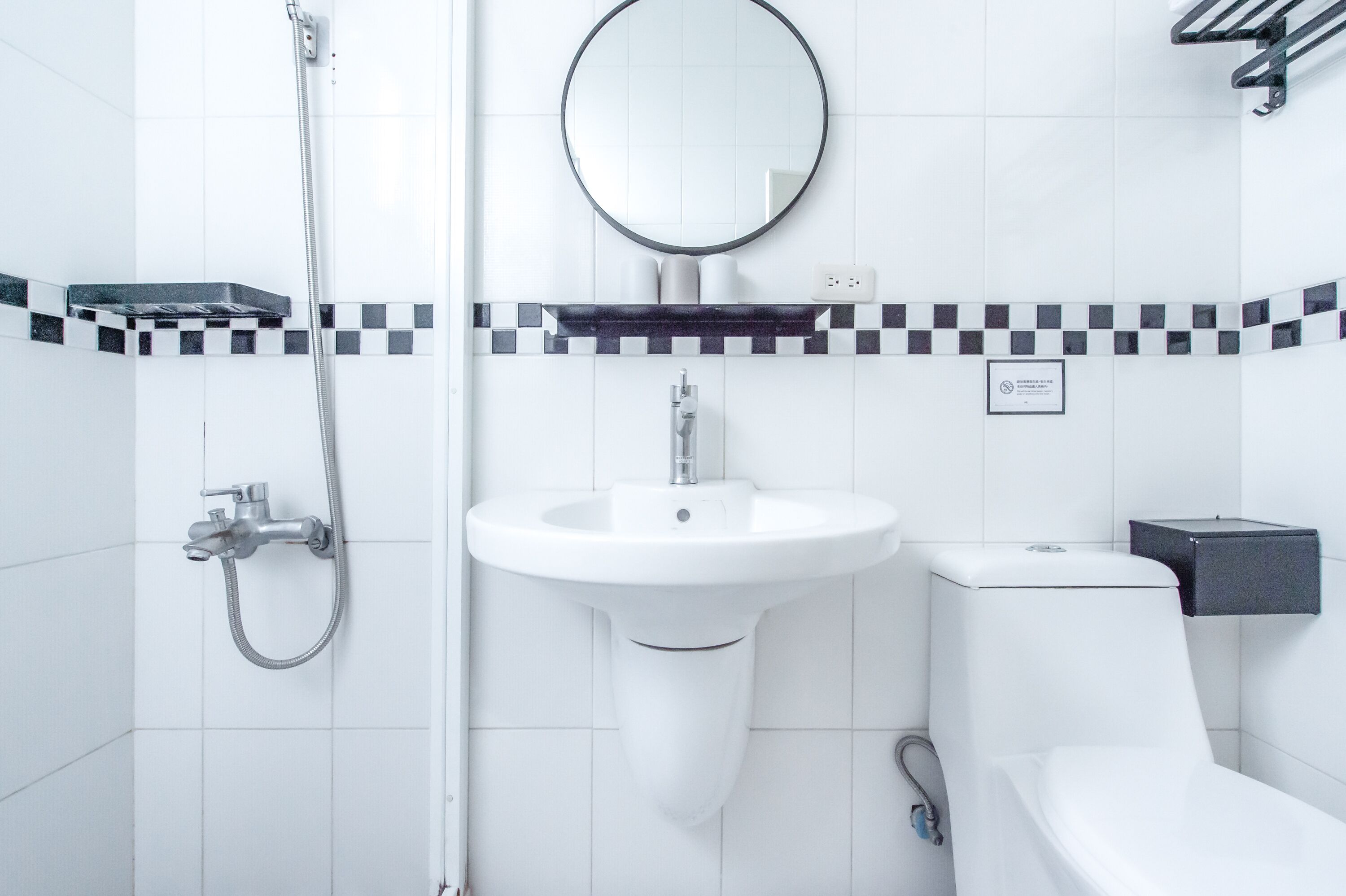 A modern bathroom with a white sink, a round mirror, a shower, and a toilet.