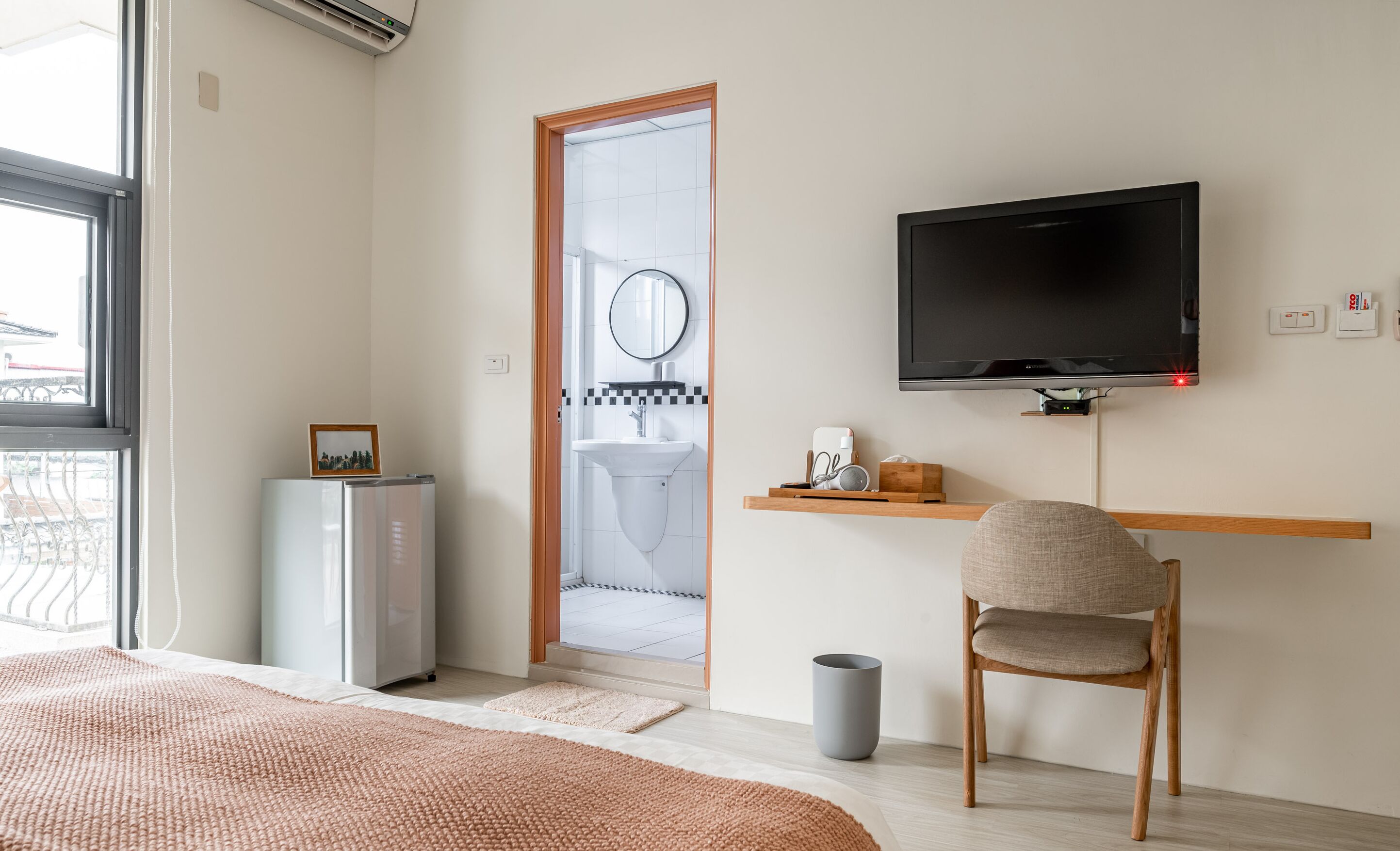 Een moderne hotelkamer met een bed, een televisie, een kleine koelkast, een wastafel en een stoel.