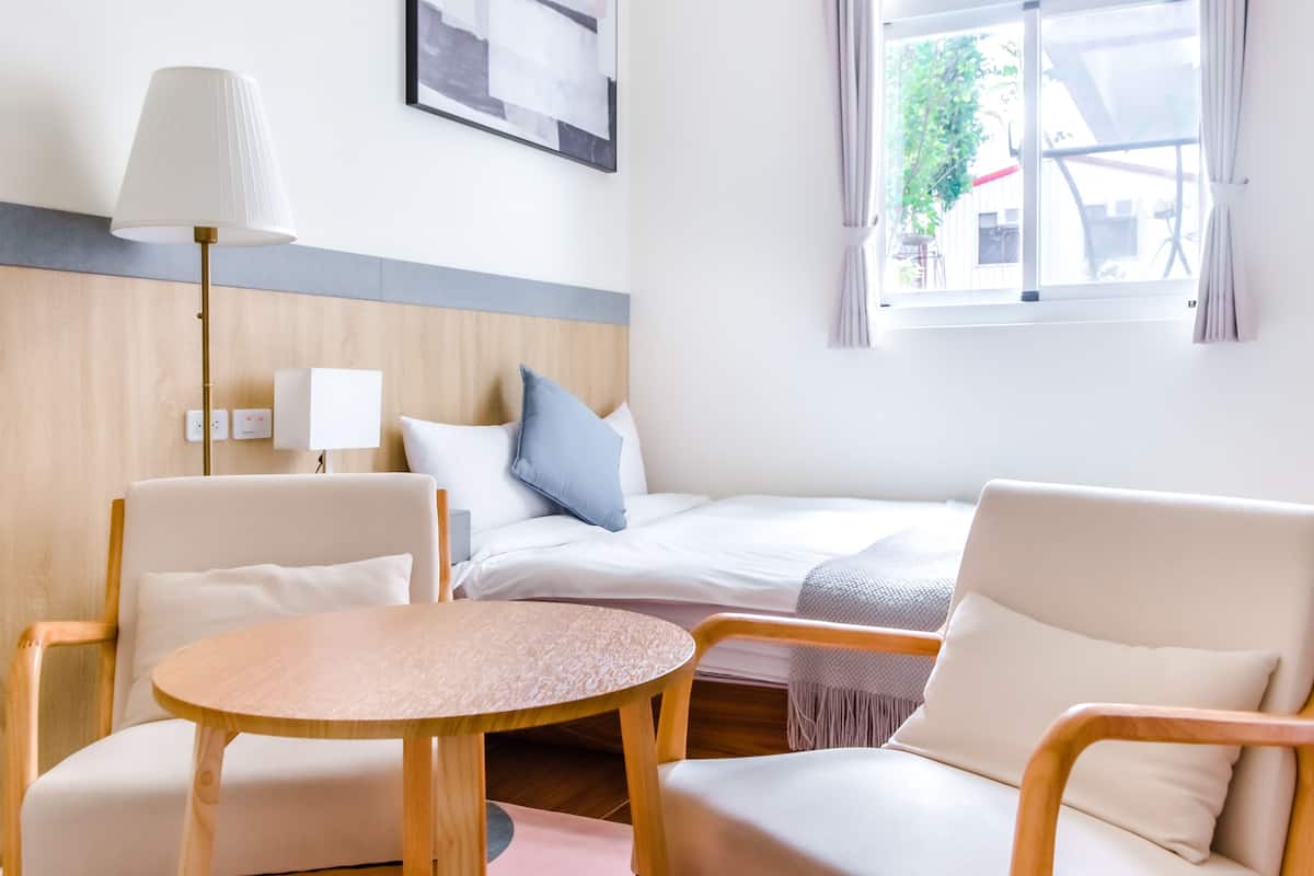 A hotel room with a bed, two chairs, a round table, a lamp, and a window with curtains.