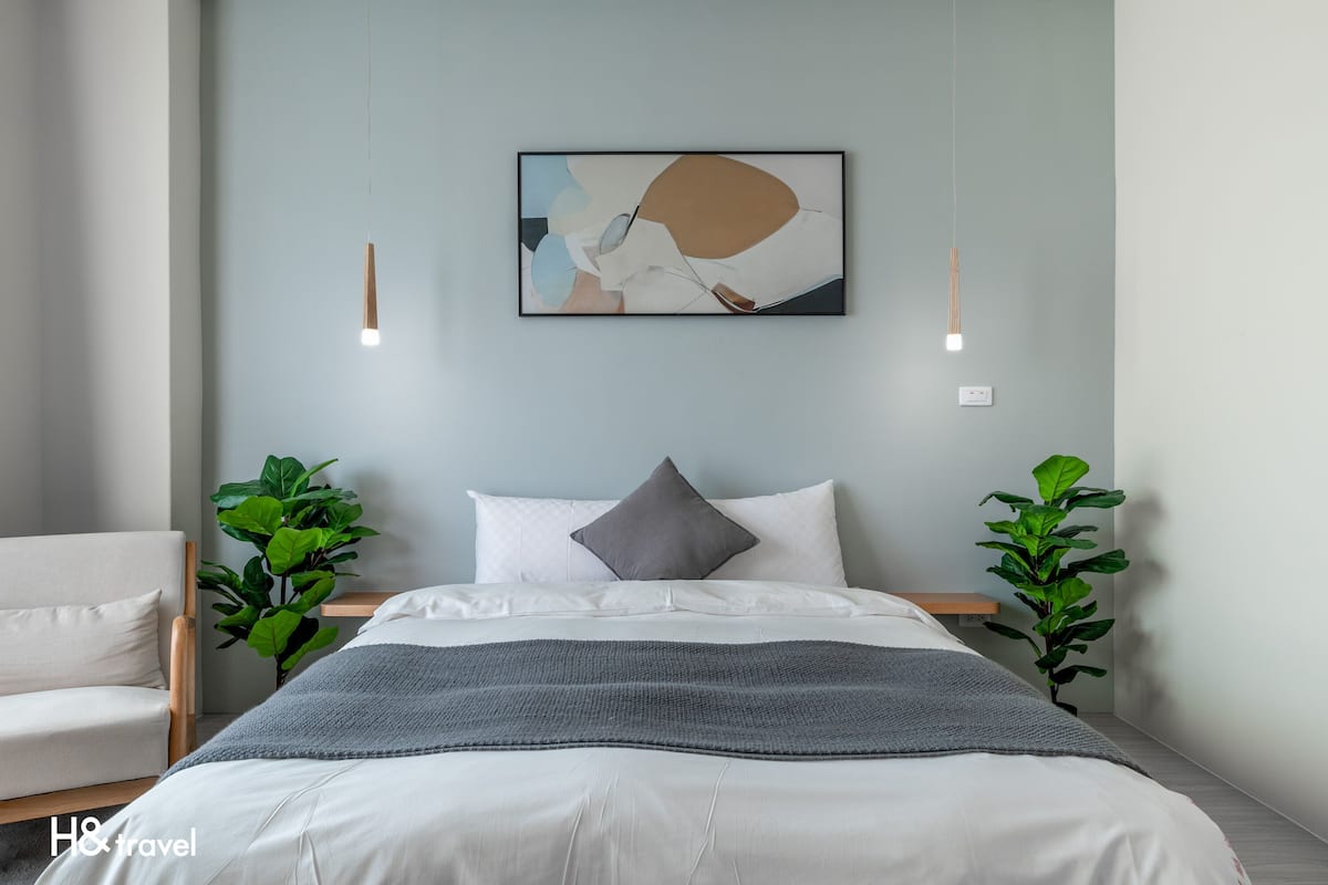A modern bedroom with a bed, pillows, a blanket, and two plants.