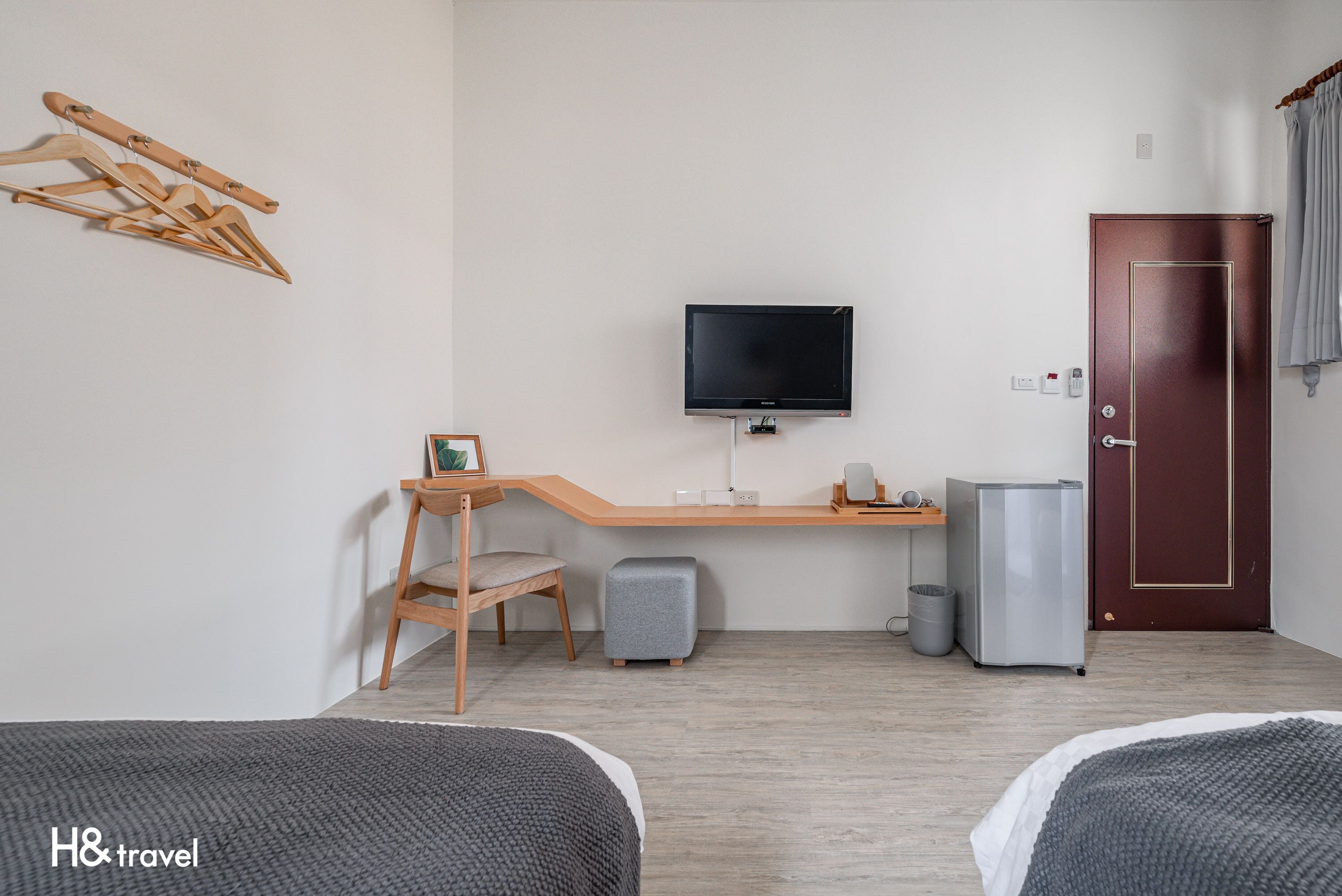 A hotel room with a wooden desk, a television, a bed, a small stool, and a door.