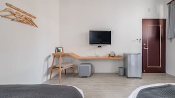 Habitación de hotel con un escritorio de madera, televisor, cama, un taburete pequeño y una puerta.