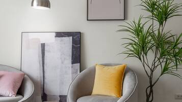 A modern living room with a grey armchair, a yellow pillow, a large abstract painting, a potted plant, and a floor lamp.