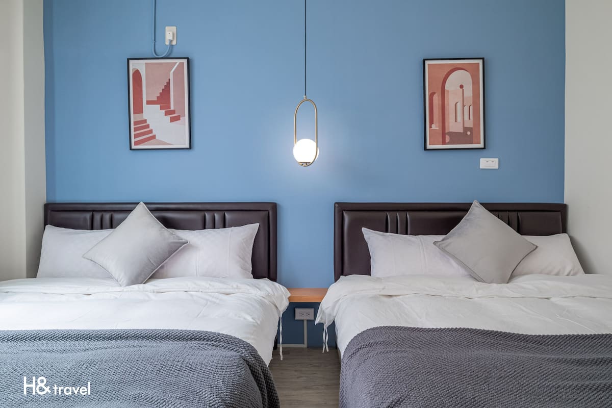 A hotel room with two beds, a blue wall, and framed artwork.