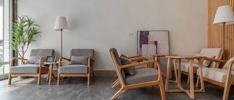 A modern hotel room with a grey sofa set, a wooden coffee table, and a large window with a view.
