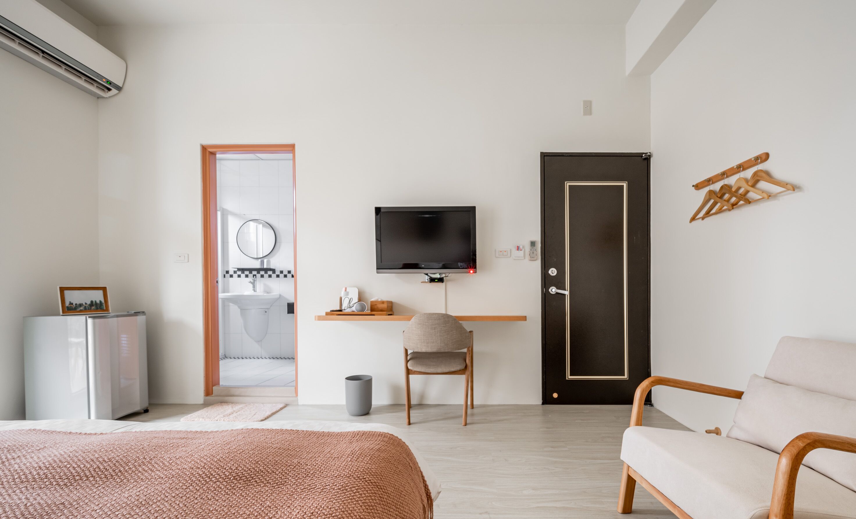 A modern bedroom with a bed, a desk with a TV, a chair, a wardrobe, and a door.