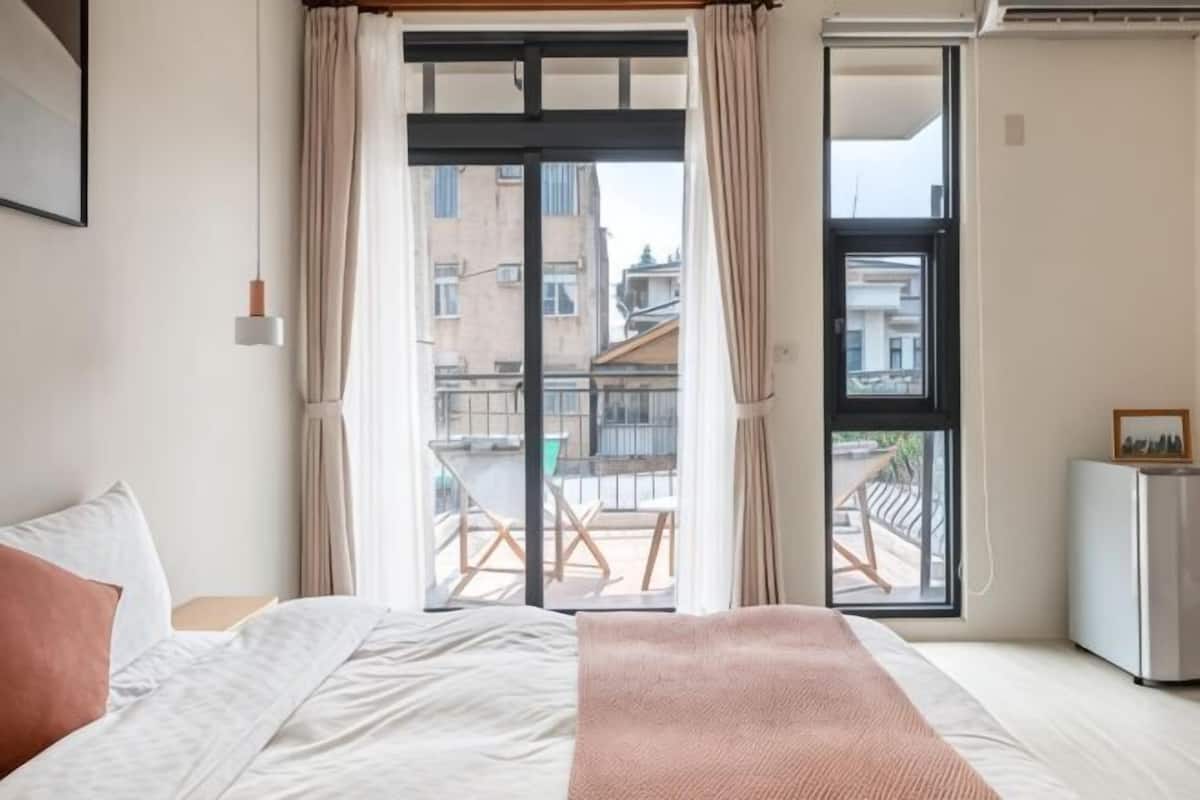 A bedroom with a bed, a bedside table, a small cabinet, and a sliding glass door leading to a balcony with outdoor furniture.