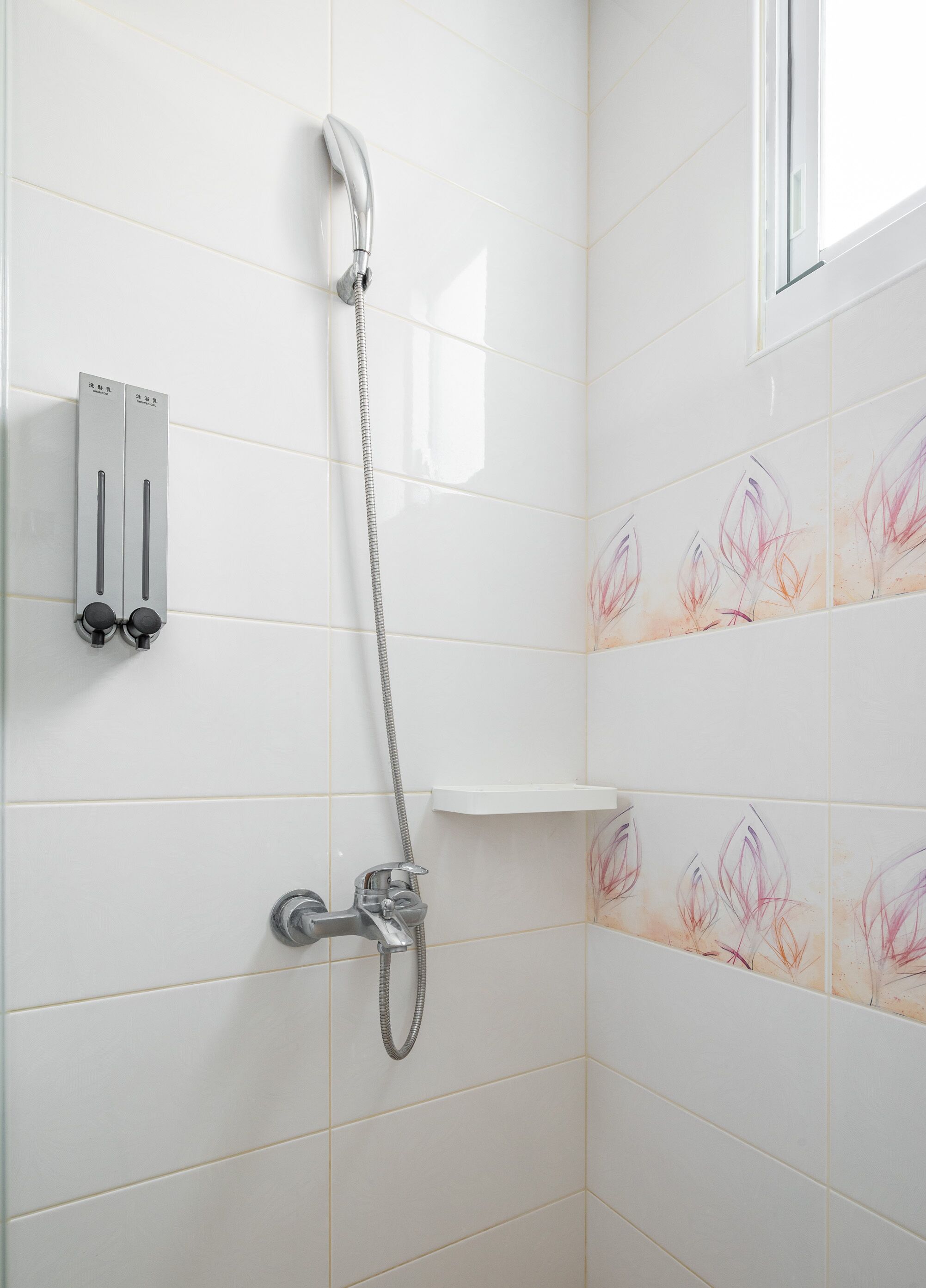 A shower area with a handheld showerhead, a wall-mounted control panel, and decorative tiles.