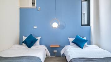 Quarto de hotel com duas camas, um espelho redondo, ar condicionado, uma janela e uma pequena mesa.