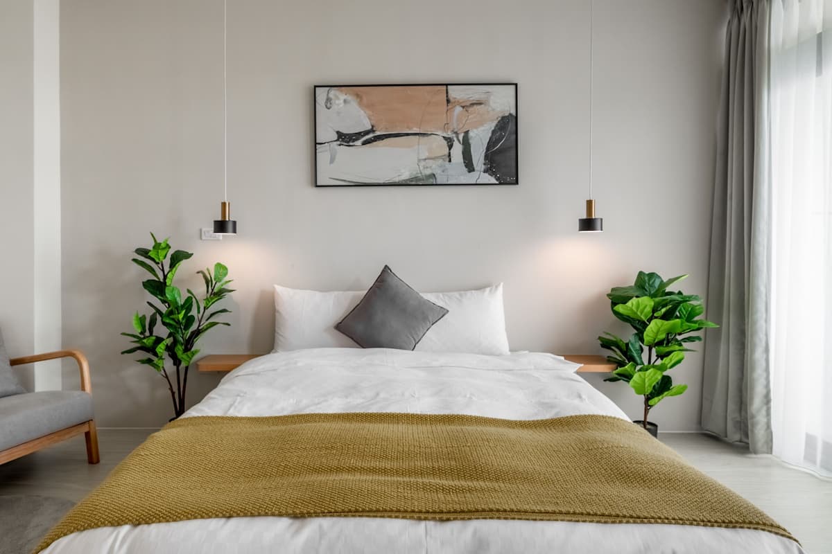 A modern bedroom with a large bed, two bedside tables, a grey armchair, and a painting on the wall.