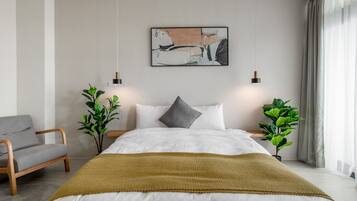 Ein modernes Schlafzimmer mit einem großen Bett, zwei Nachttischen, einem grauen Sessel und einem Bild an der Wand.