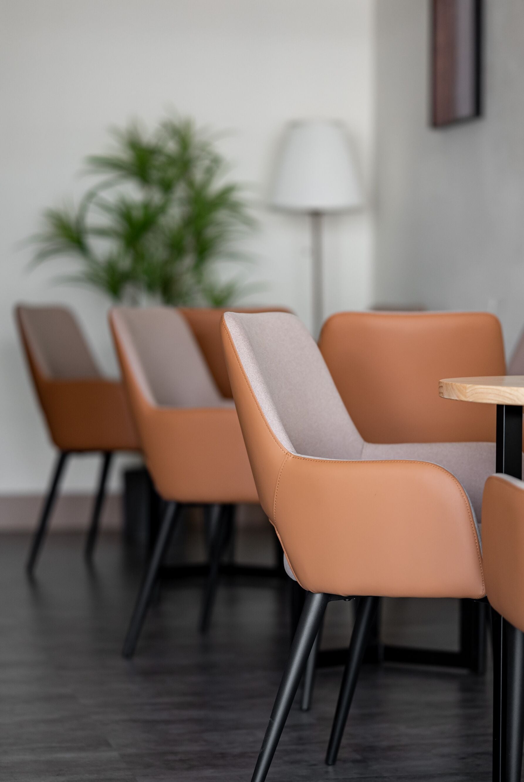 Una hilera de sillas modernas con una paleta de colores marrón claro y gris, ubicadas en una habitación con piso de madera oscura y una lámpara blanca al fondo.