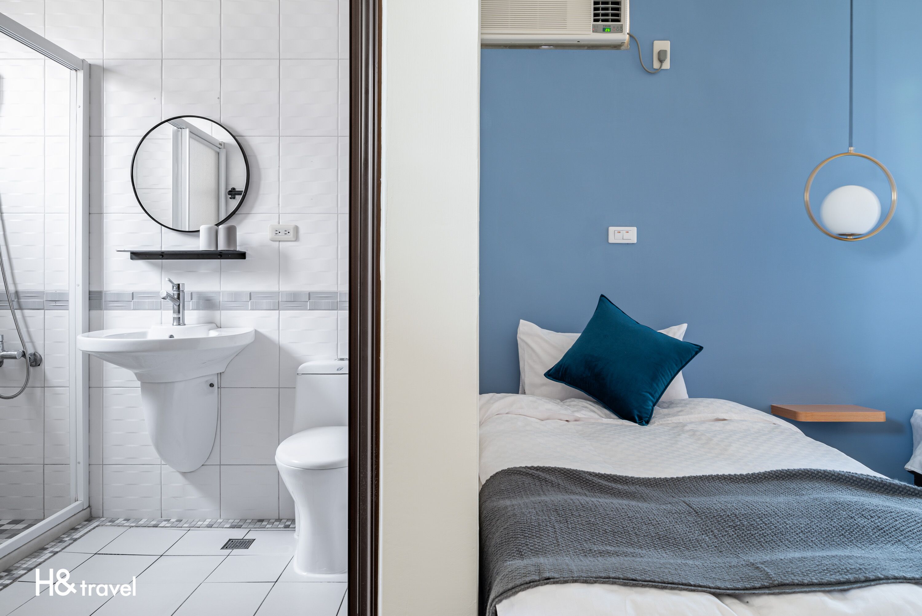Une salle de bain moderne avec un lavabo, des toilettes et un miroir. La pièce a un mur bleu et un lit avec un oreiller bleu.