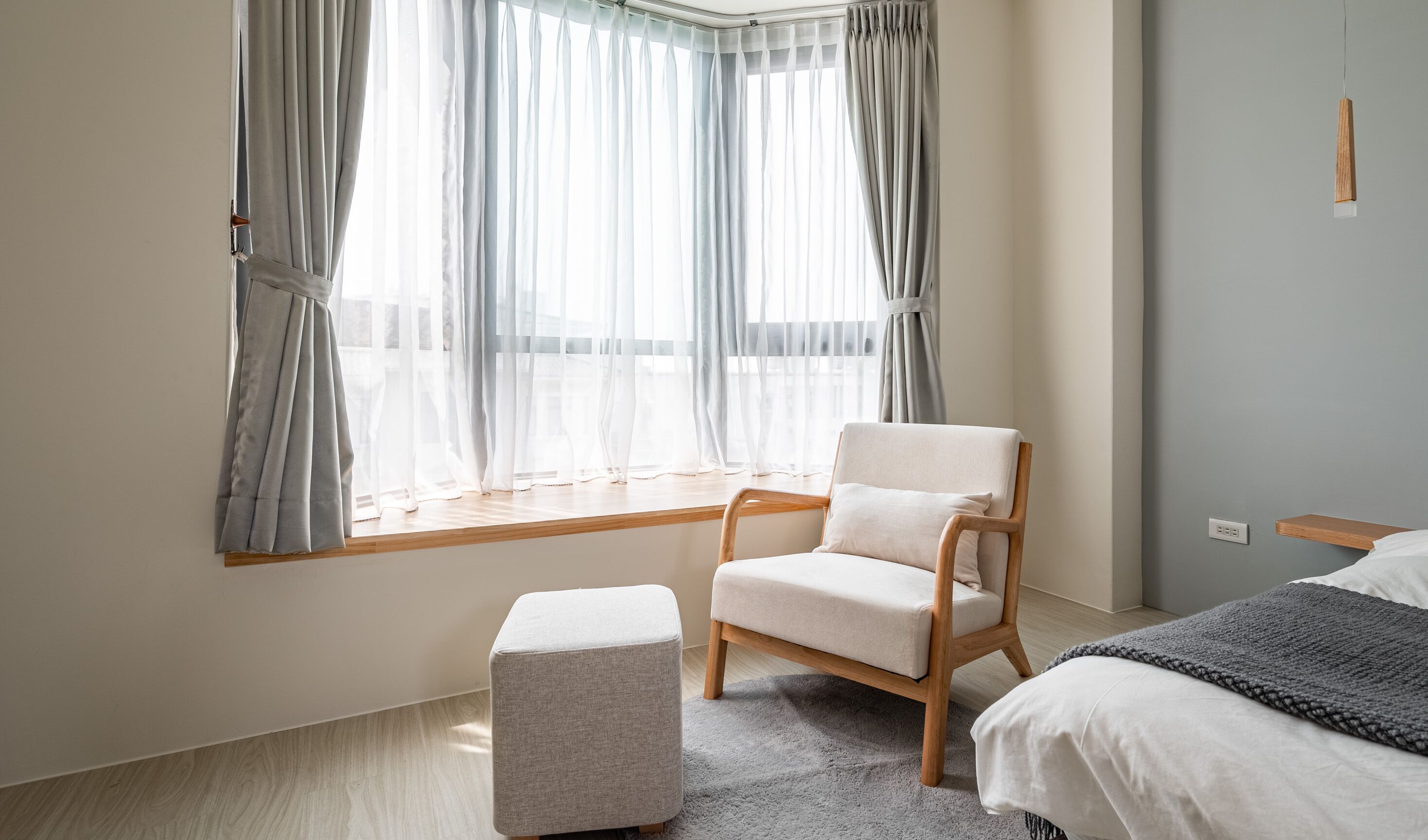 A modern bedroom with a large window, a wooden chair, a bedside table, and a bed.