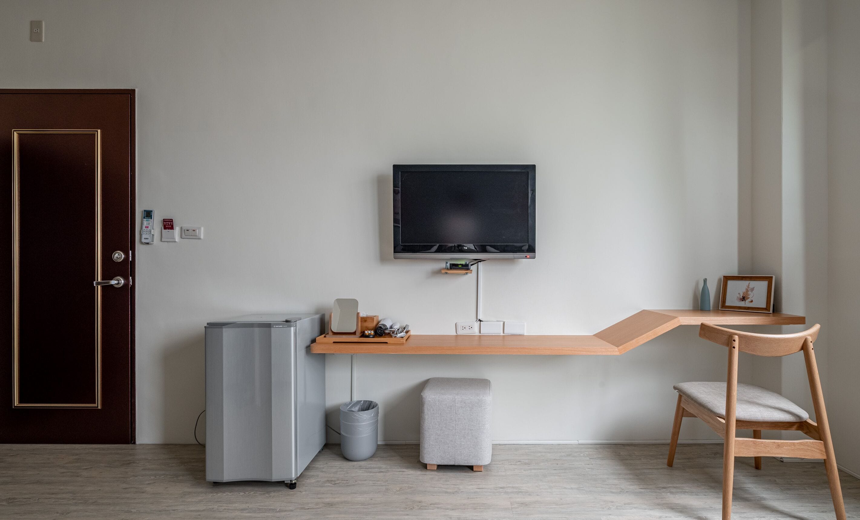 Una habitación moderna con escritorio, televisión, refrigerador, basurero y una silla.