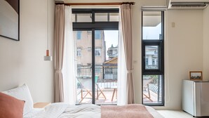 Een hotelkamer met een bed, een klein bureau, een koelkast en uitzicht op het balkon.