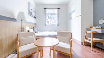 A hotel room with a bed, two chairs, a small table, a lamp, and a window with curtains.