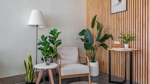 Een moderne woonkamer met een witte fauteuil, een vloerlamp en verschillende potten met planten.