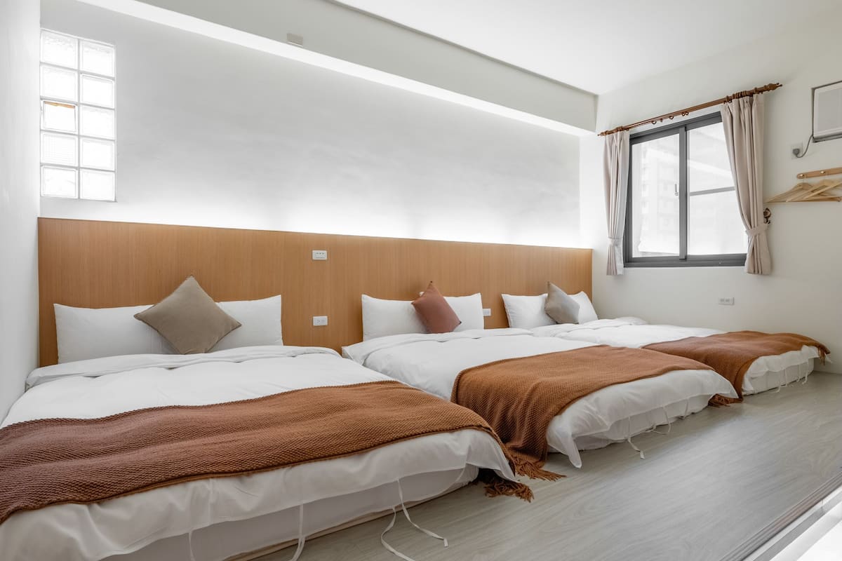 A hotel room with two beds, a wooden headboard, a window with curtains, and a light-colored floor.