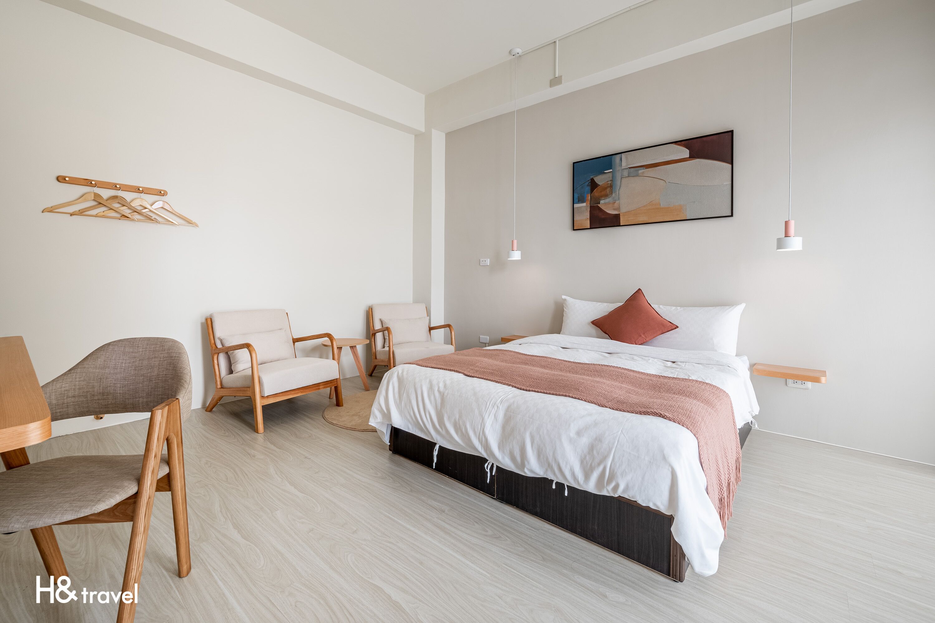 A modern hotel room with a bed, two chairs, a desk, and a hanging coat rack.