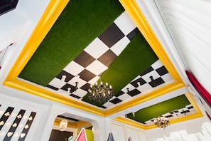 Una habitación con techo a cuadros, césped artificial verde, candelabros y una pared decorada con símbolos de cartas de juego.