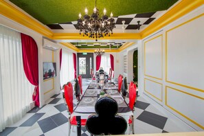 Un comedor con piso de tablones de ajedrez, cortinas rojas y una araña.