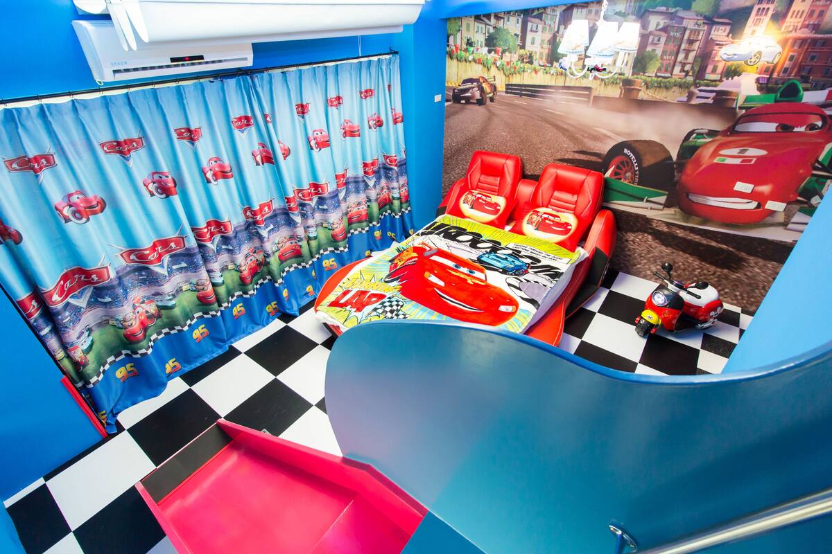 Quarto infantil com tema de carros de corrida, incluindo uma cama com edredom de carro de corrida, piso xadrez e um mural de pista de corrida.