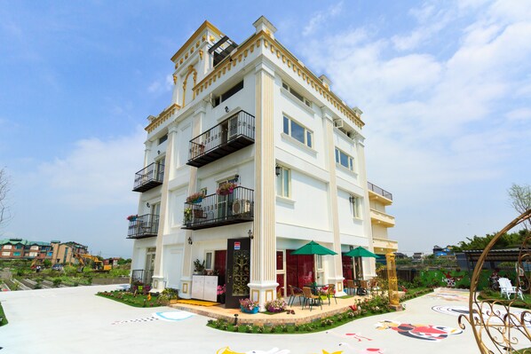 Un hotel de varios pisos con balcones, mobiliario exterior y un jardín.