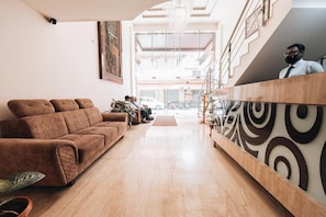 A reception area with a brown sofa, a wooden reception desk, and a staircase leading to an upper level.