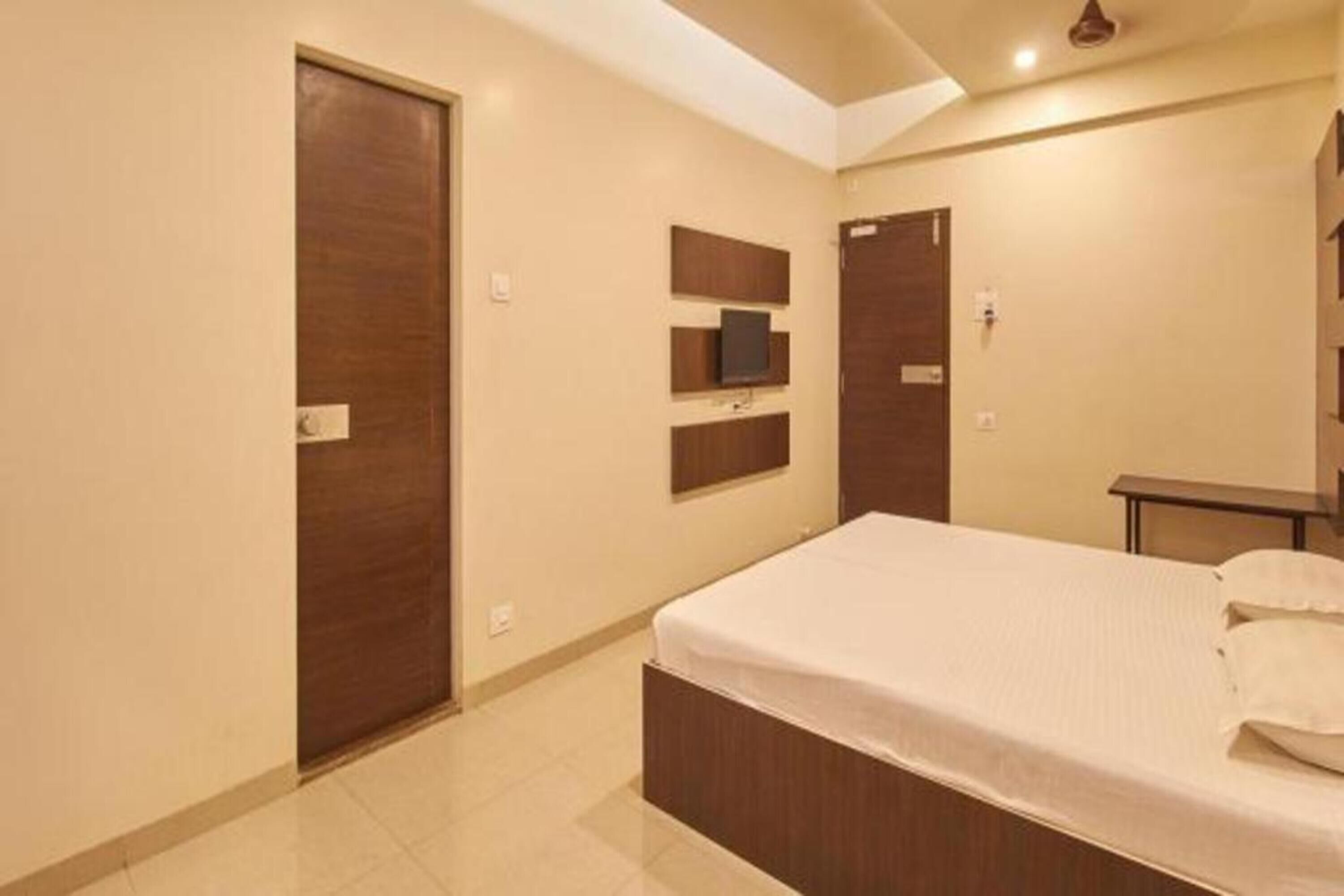 A bedroom with a bed, a wardrobe, a TV mounted on the wall, and a small table.