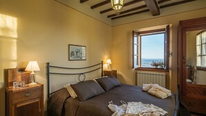 A bedroom with a bed, nightstands, a lamp, a window with a view, and a wooden ceiling.