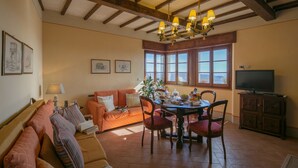 A cozy living room with a wooden ceiling, a dining area with a table and chairs, and a television on a cabinet.