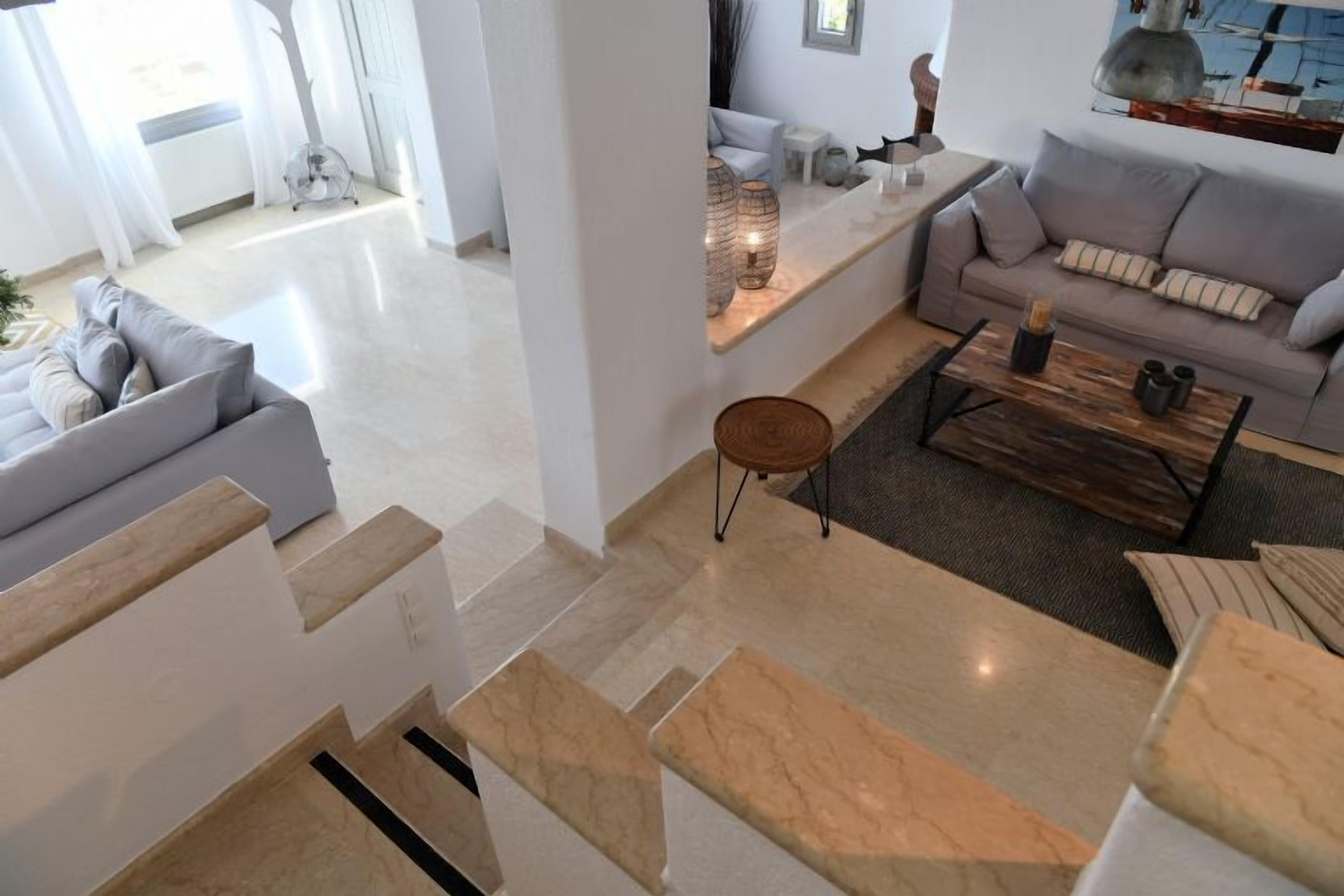 Un salon moderne avec un canapé gris, une table basse et un escalier recouvert de carreaux beiges et blancs.