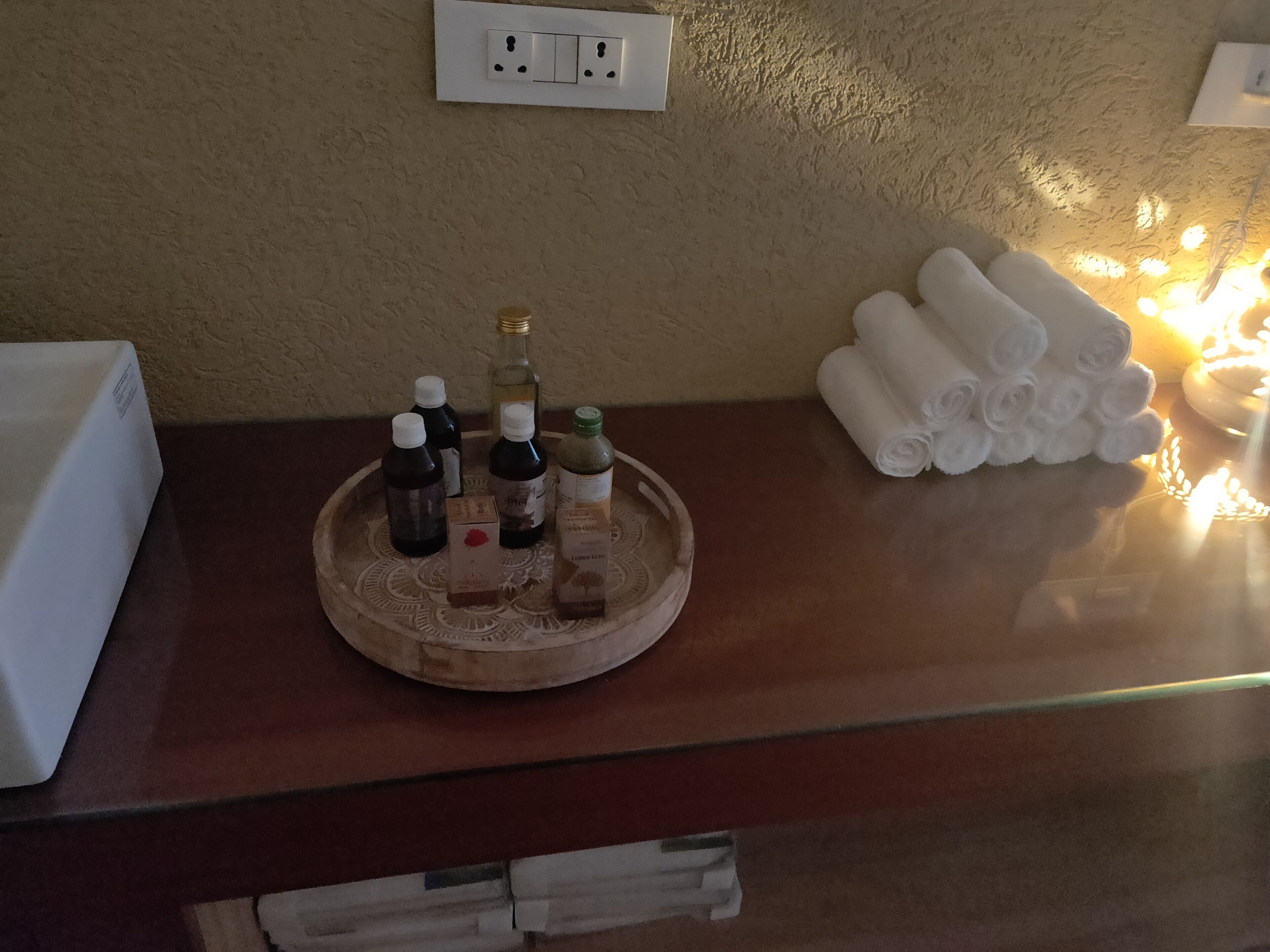 A wooden tray with various bottles on a counter, a white box, and rolled towels.